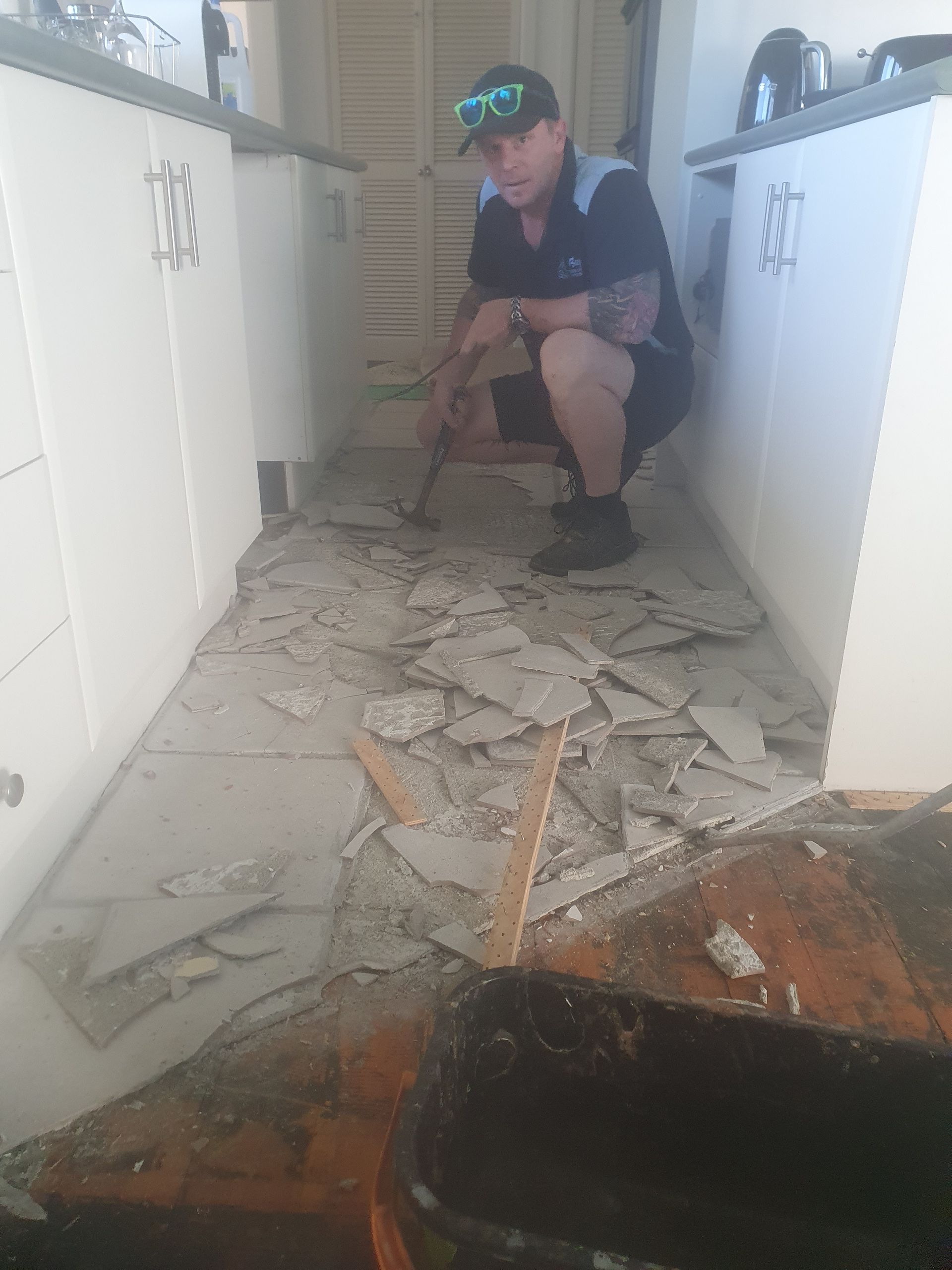 A man is kneeling on the floor of a kitchen. A man is kneeling on the floor of a kitchen.