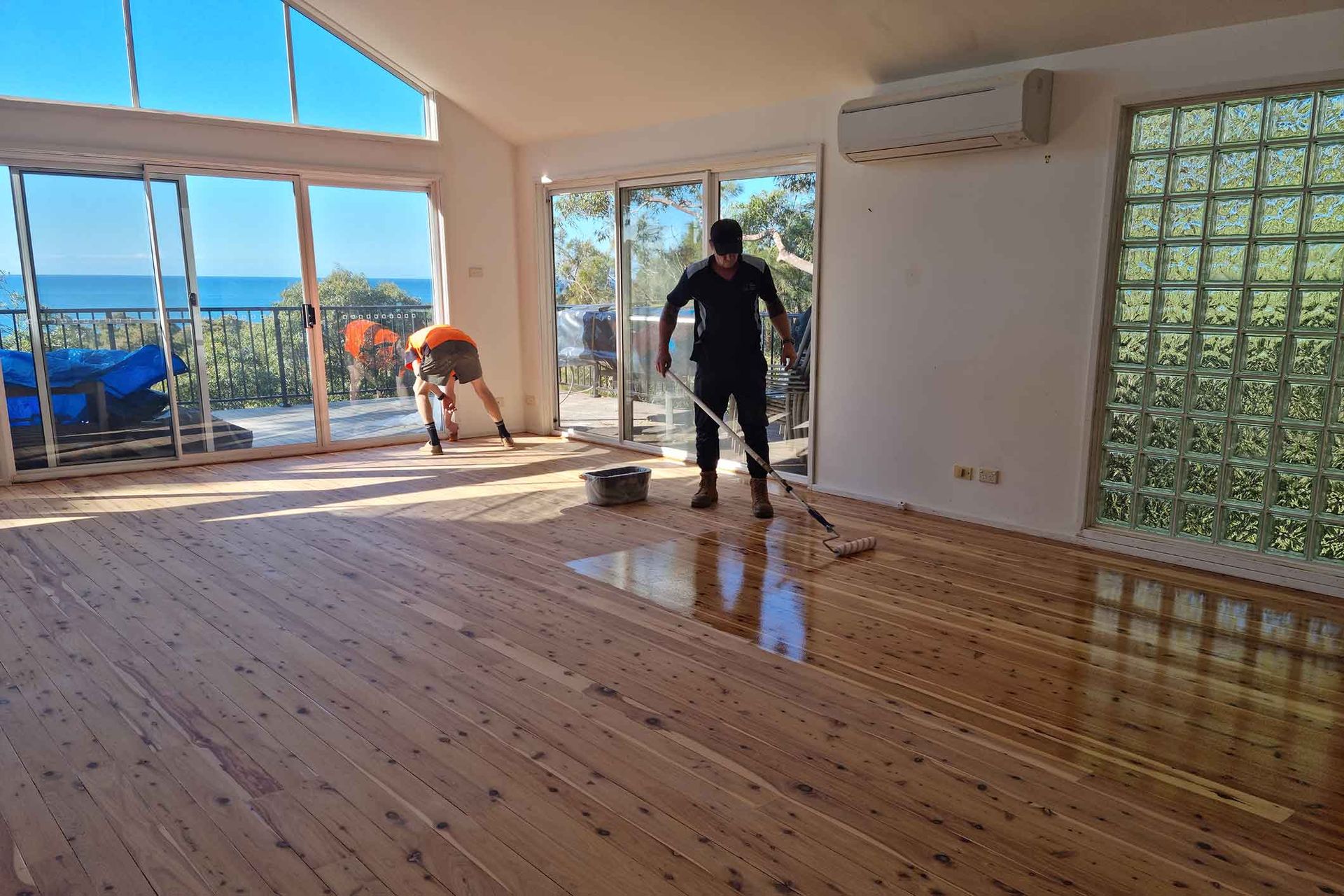 A man is painting a wooden floor in a living room. A man is painting a wooden floor in a living room.