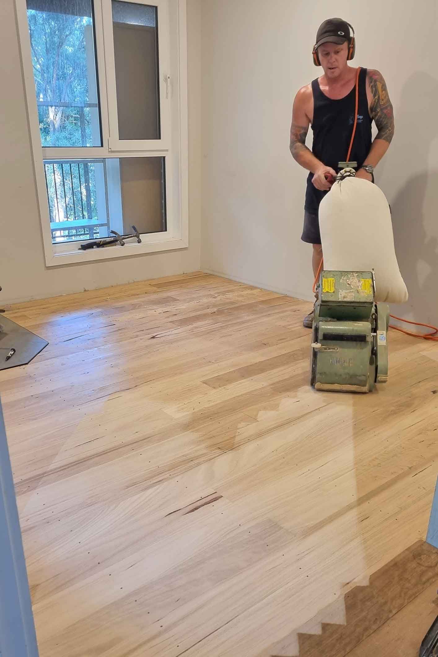A man is sanding a wooden floor with a machine. A man is sanding a wooden floor with a machine.