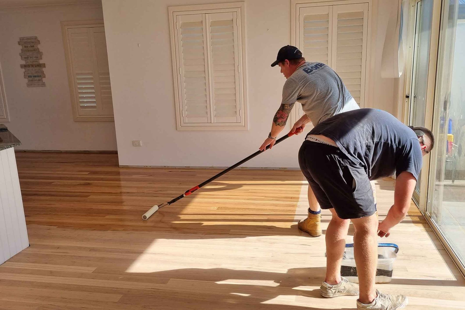Two men are painting a wooden floor with a roller. Two men are painting a wooden floor with a roller.