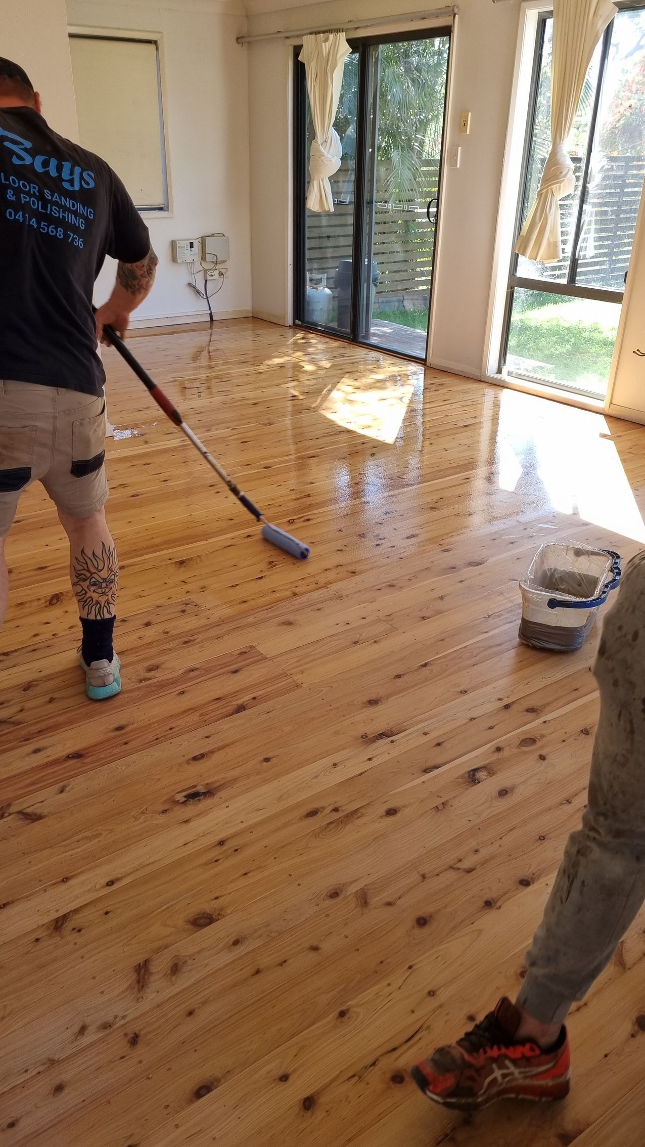 A man is painting a wooden floor in a living room. A man is painting a wooden floor in a living room.