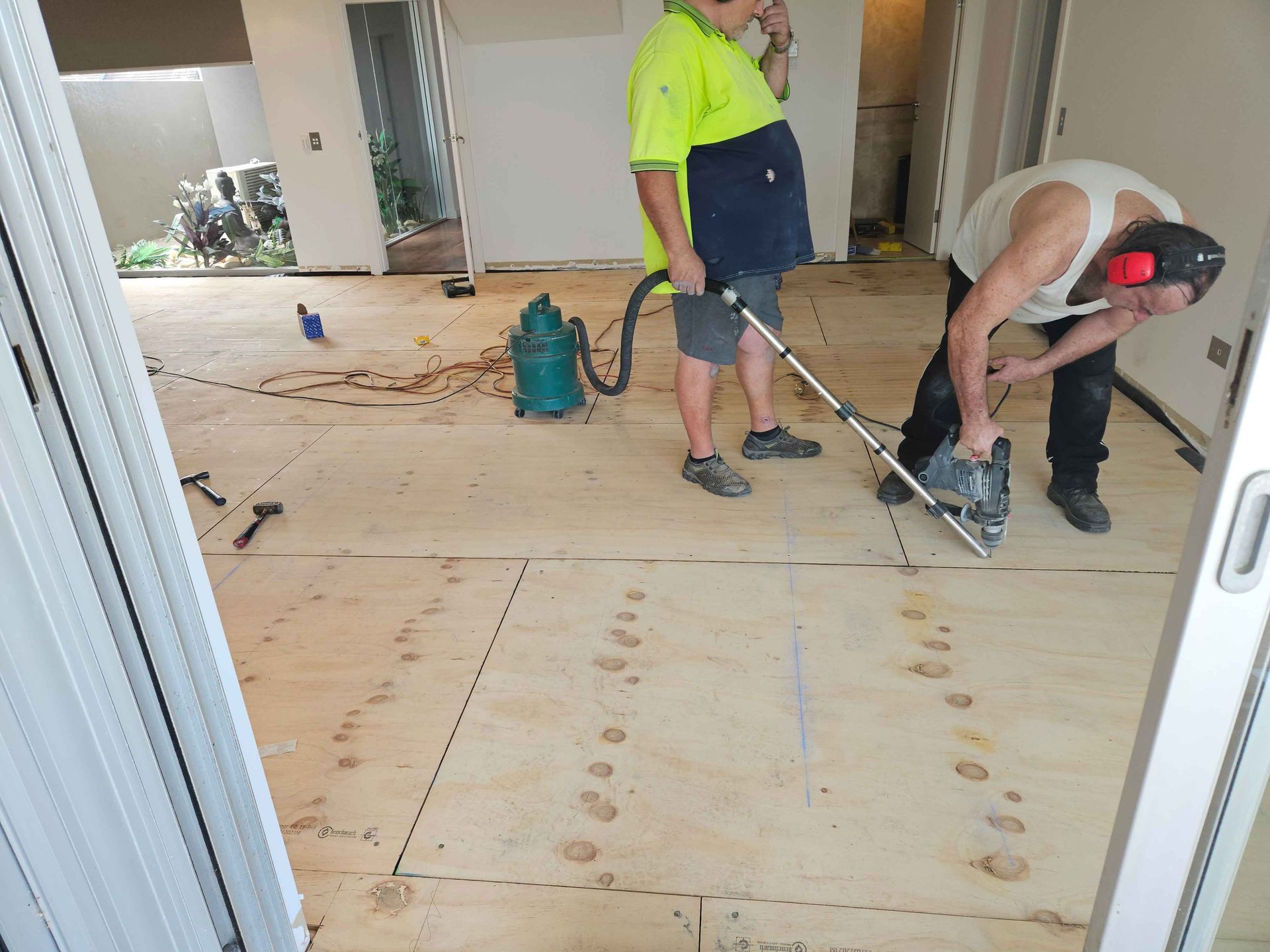 Two men are working on a wooden floor with a vacuum cleaner