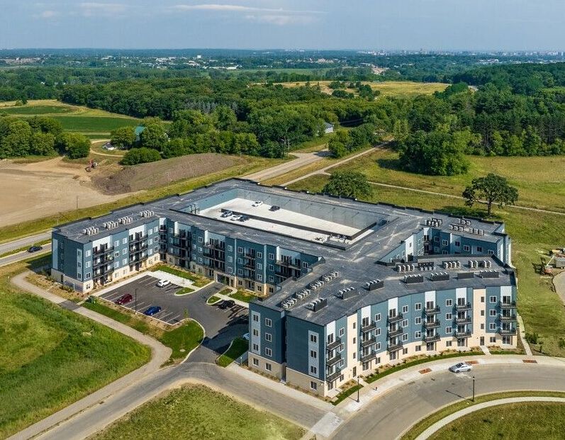 An aerial view of a large apartment building surrounded by fields and trees.