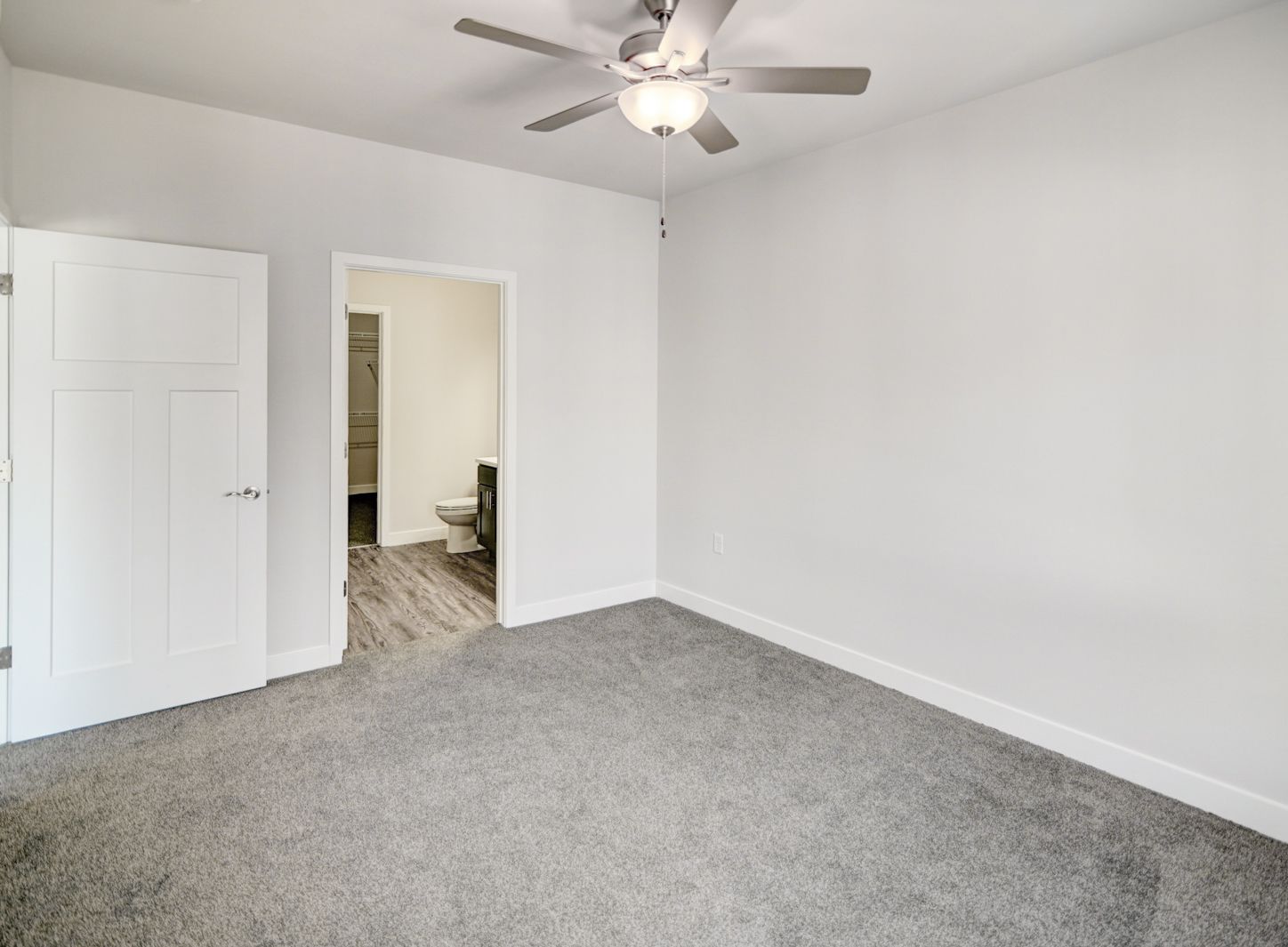 An empty bedroom with a ceiling fan and a toilet.
