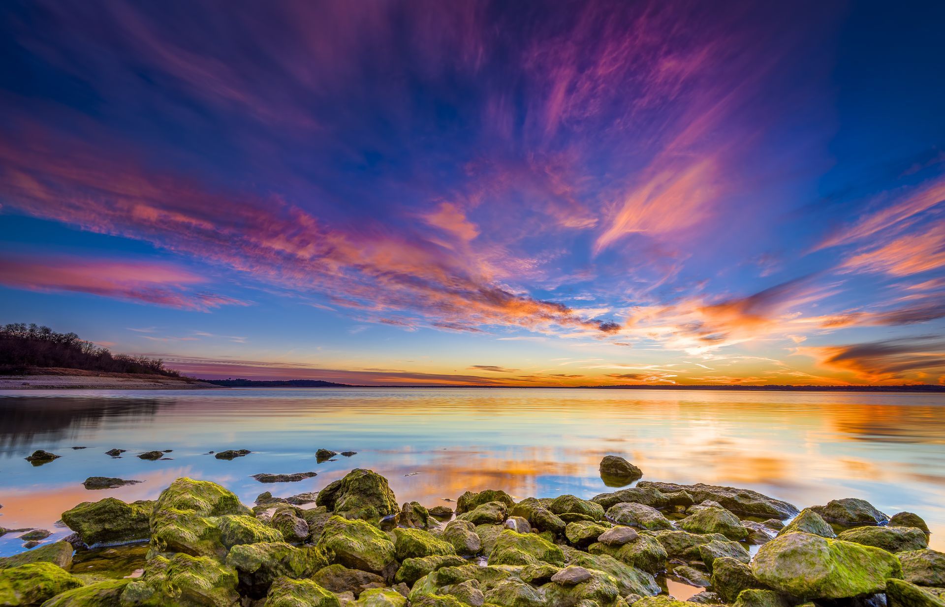 A sunset over a body of water with rocks in the foreground.