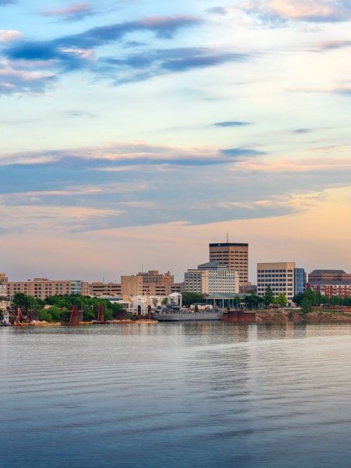 A wooden walkway leading to a gazebo overlooking a body of water at sunset.