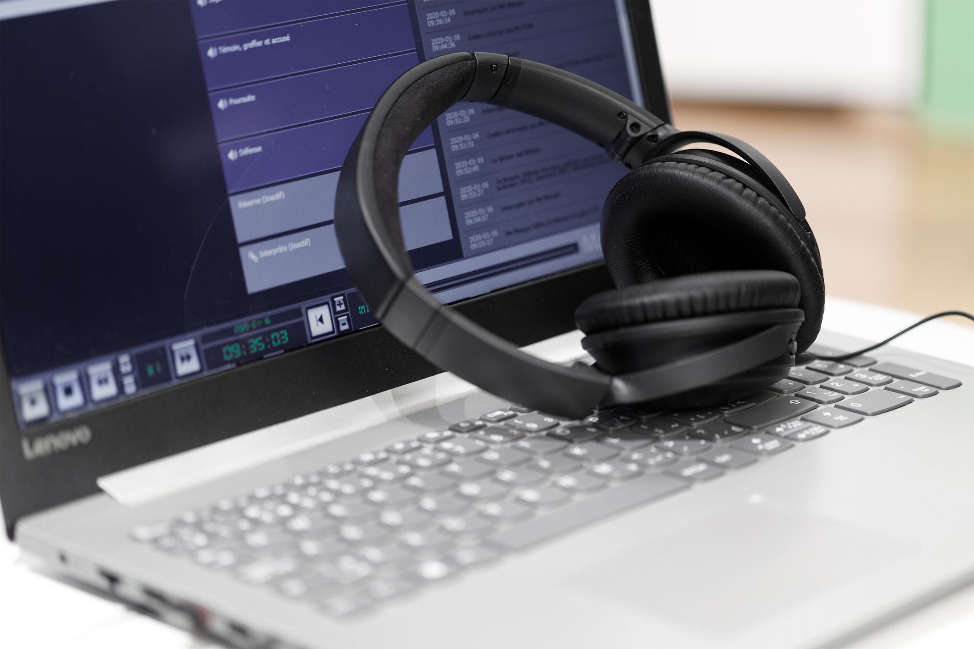 Un casque audio noir repose sur le clavier d'un ordinateur portable ; le logiciel audio est visible à l'écran.