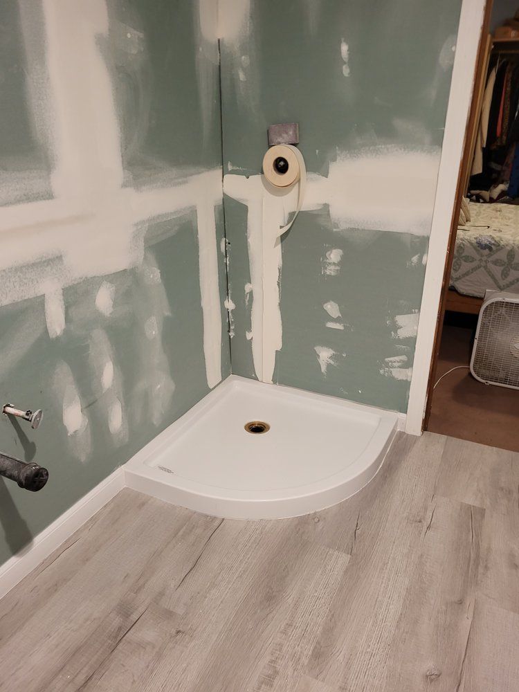 Renovated bathroom shower corner with green drywall, white shower base, and gray wood-look floor.