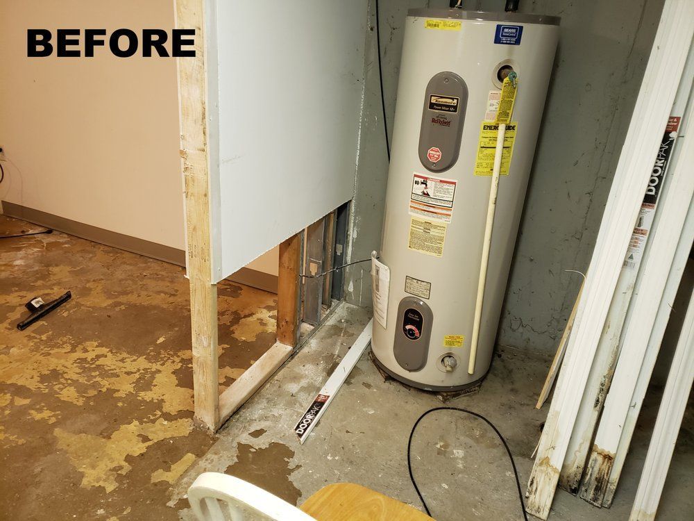 Before photo of a bathroom under renovation with exposed wall framing and a water heater visible.