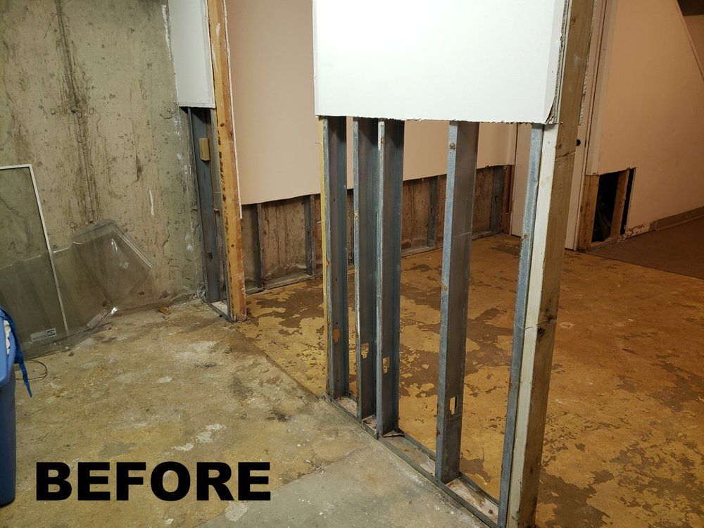Basement renovation before photo showing exposed studs, drywall, and concrete floor.