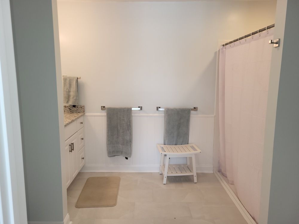 Minimal bathroom with white walls, gray towels, a bench, sink cabinet, and shower curtain.