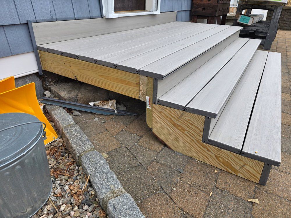 Outdoor gray deck steps with black trim beside a house and trash can