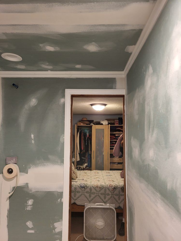 Partially painted room with green walls, white ceiling patches, and an open doorway to a cluttered closet area.