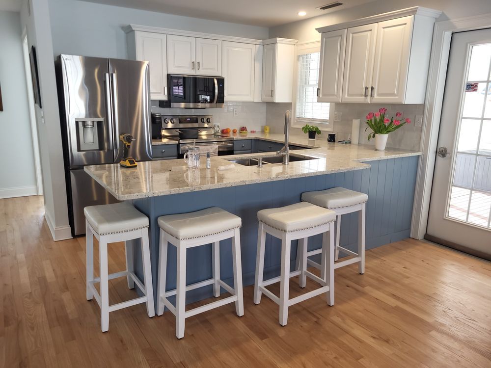 Bright kitchen with white cabinets, stainless appliances, blue island, and three stools on wood floor.