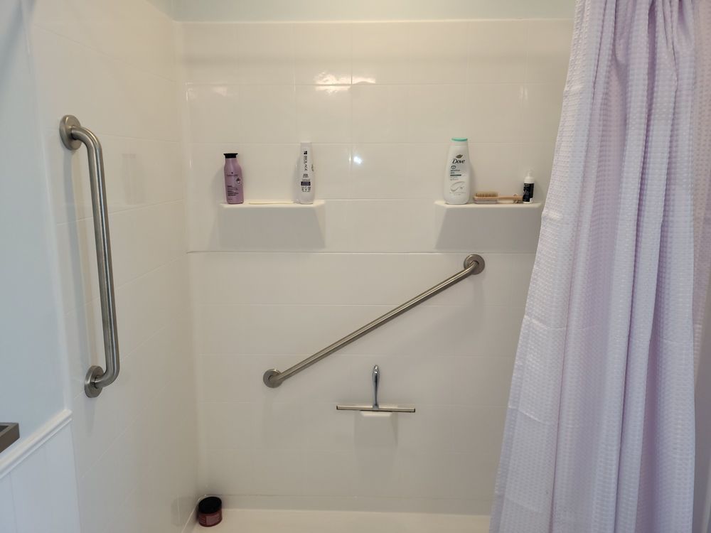 Accessible shower stall with grab bars, shower bench, and curtain in a white tiled bathroom