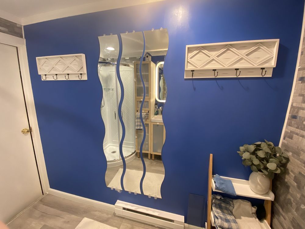 Blue entryway wall with wavy mirror, white coat hooks, and a tiled floor area