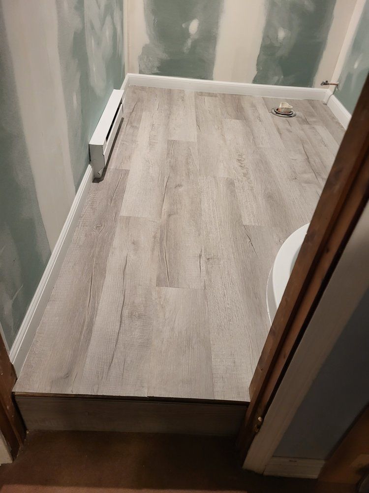 Partially finished bathroom with wood-look floor, green drywall, and a toilet opening on the right