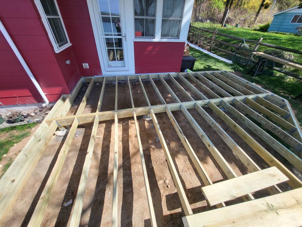 Partially built wooden deck framing beside a red house with white trim