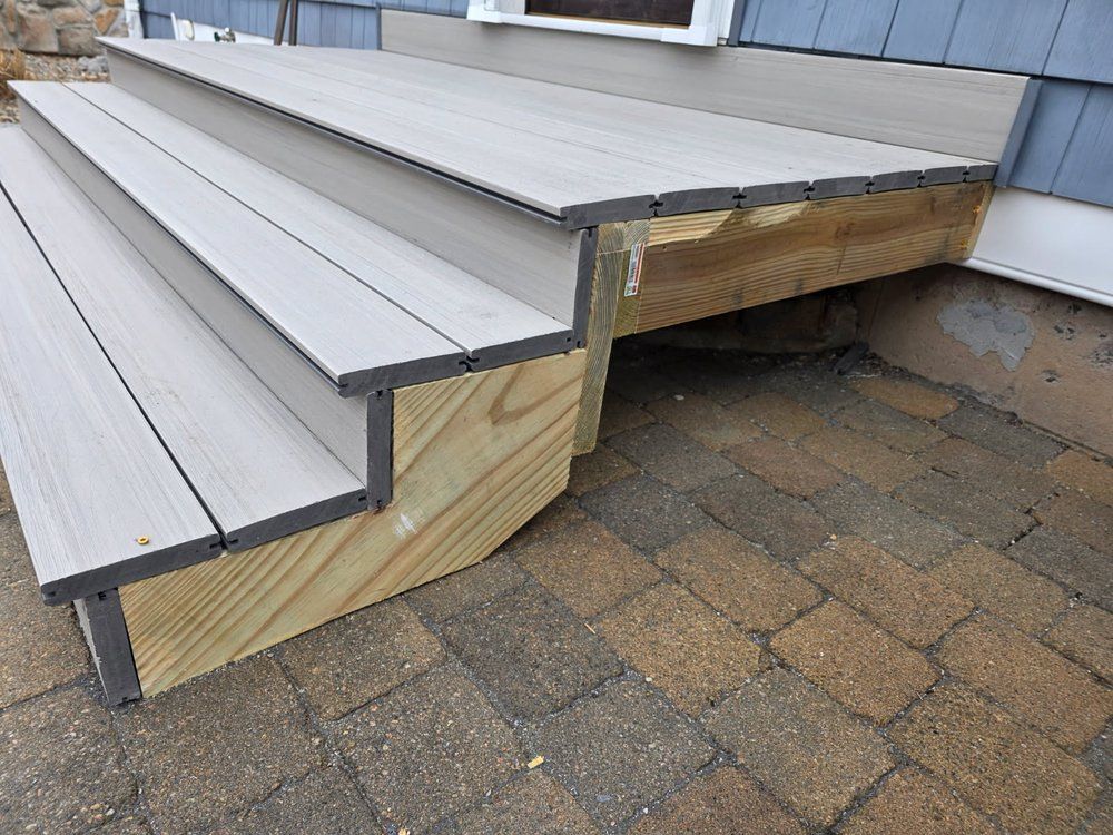 Close-up of gray stair treads with exposed wood framing on a paved patio.