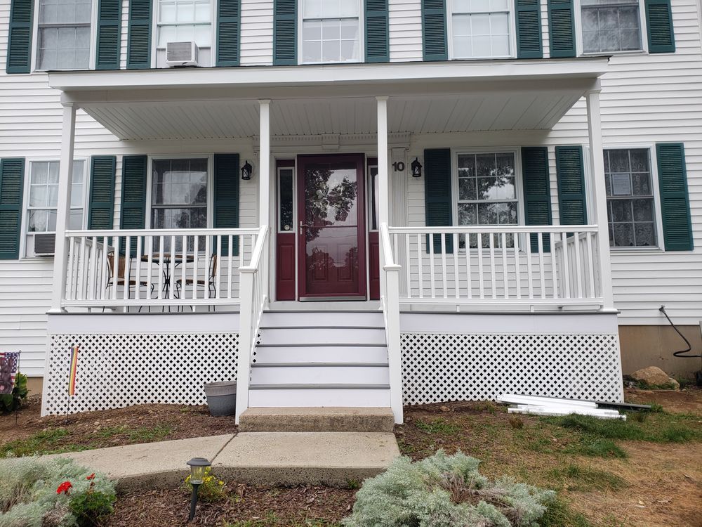 Front view of a white house with green shutters, red front door, and a small porch with white railings.