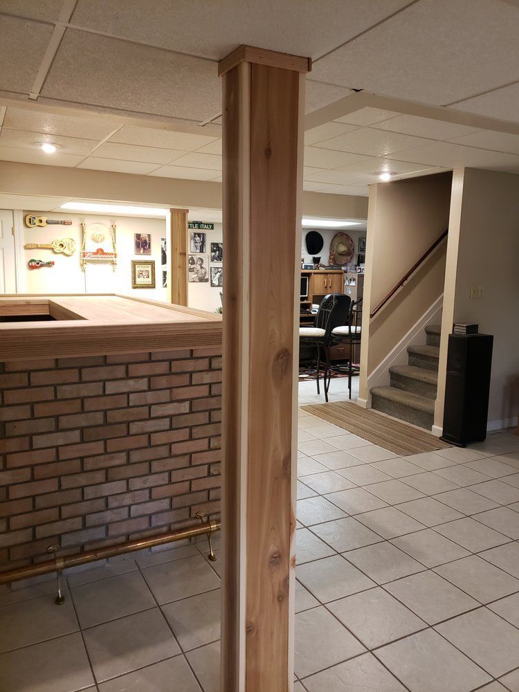 Basement lounge with brick bar, wooden support post, tiled floor, and stairs leading up.