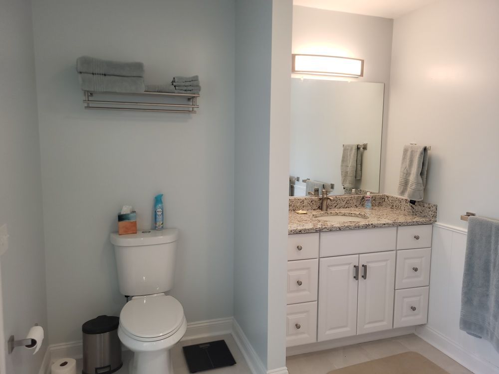 Small bathroom with toilet, vanity, mirror, granite countertop, and towels hanging on wall and radiator.