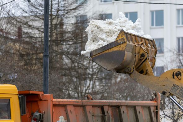 Snow-filled excavator bucket dumping into a dump truck at a construction site