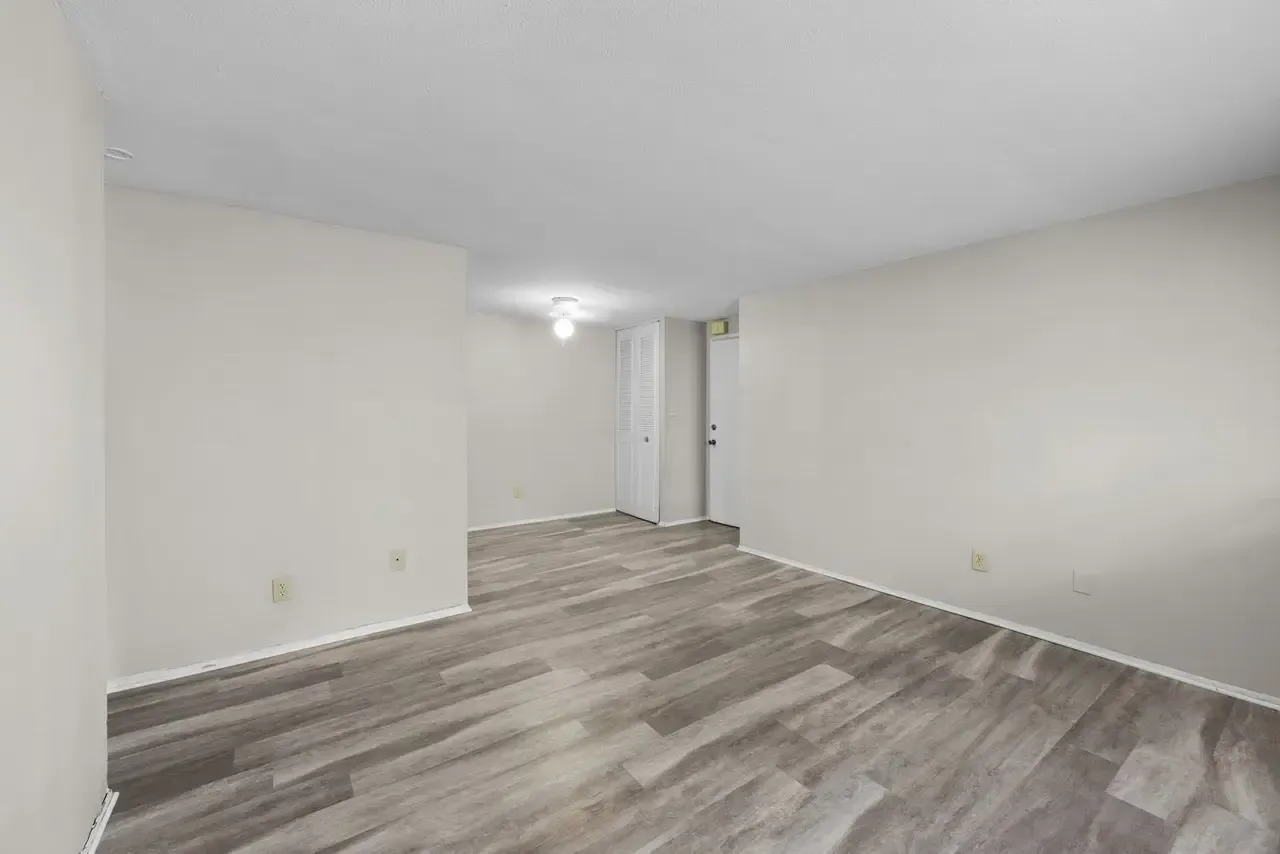 An empty room with light grey walls, white trim, and grey wood-look flooring leading to an open doorway.