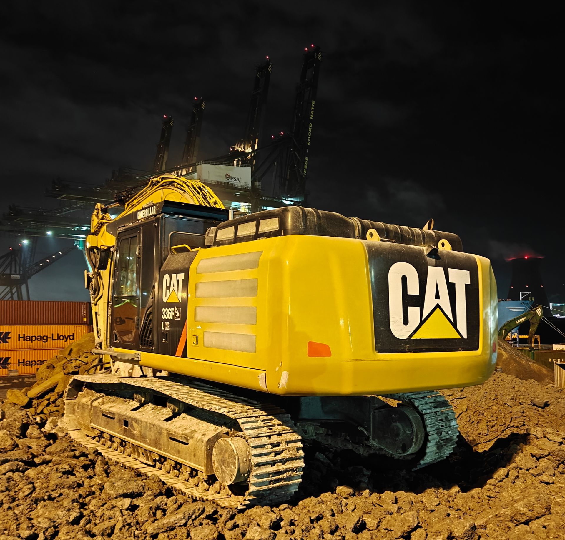 Gele CAT-rupsgraafmachine op een modderig bouwterrein 's nachts