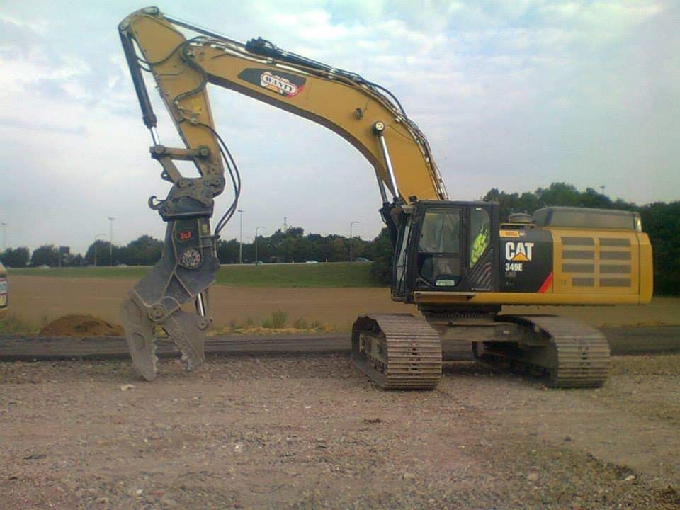 Gele CAT-graafmachine met grijper geparkeerd op een grindterrein onder een bewolkte hemel.