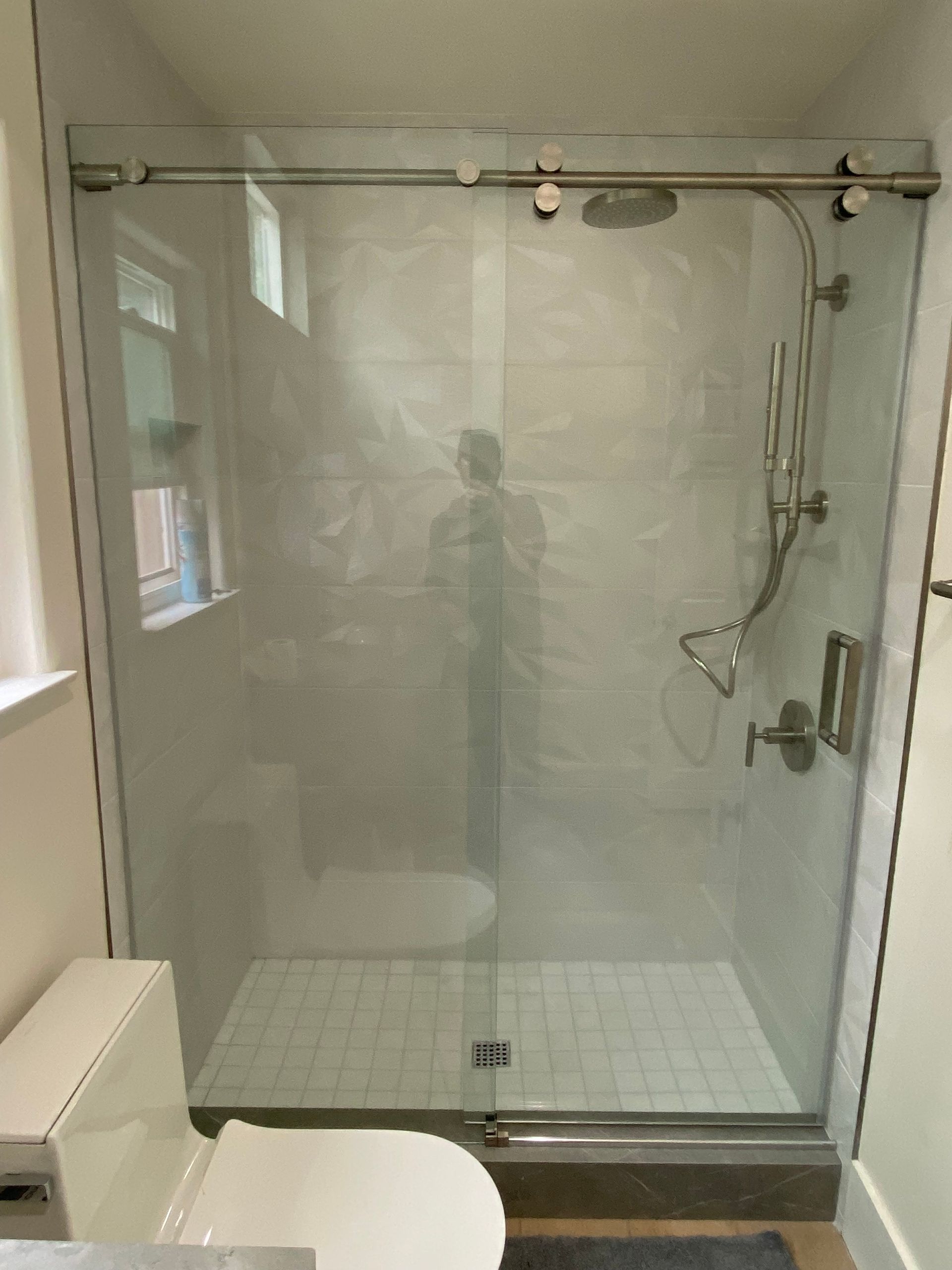 Glass shower with sliding door, white tiles, showerhead, toilet visible on the left.