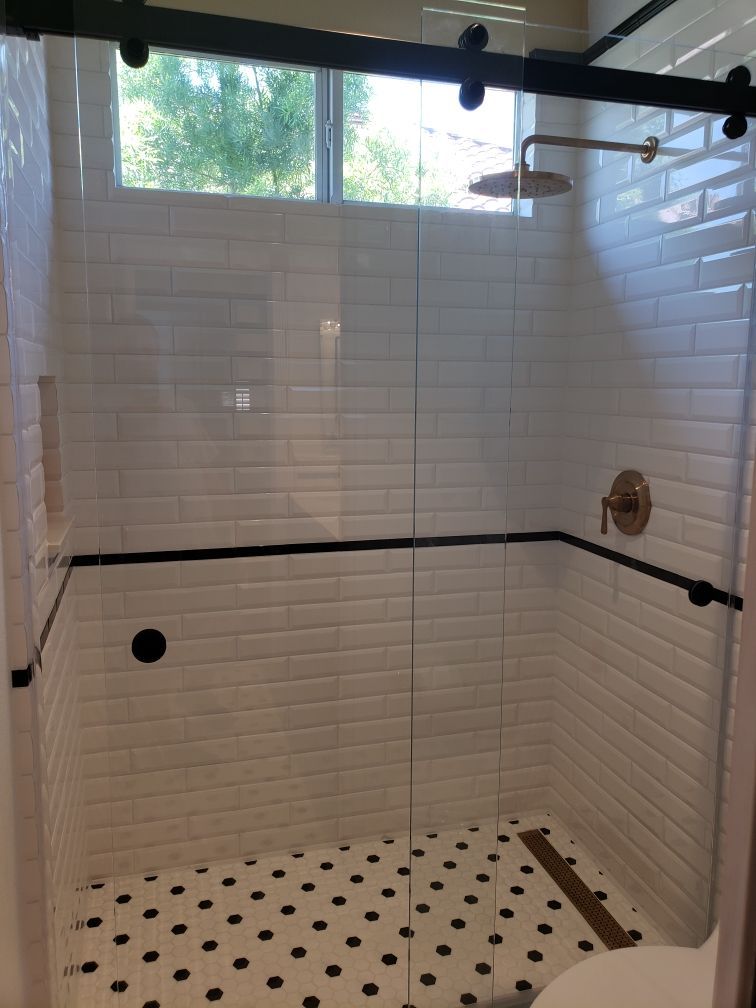 Shower with white subway tile, black and white floor tile, and gold fixtures. Glass doors.