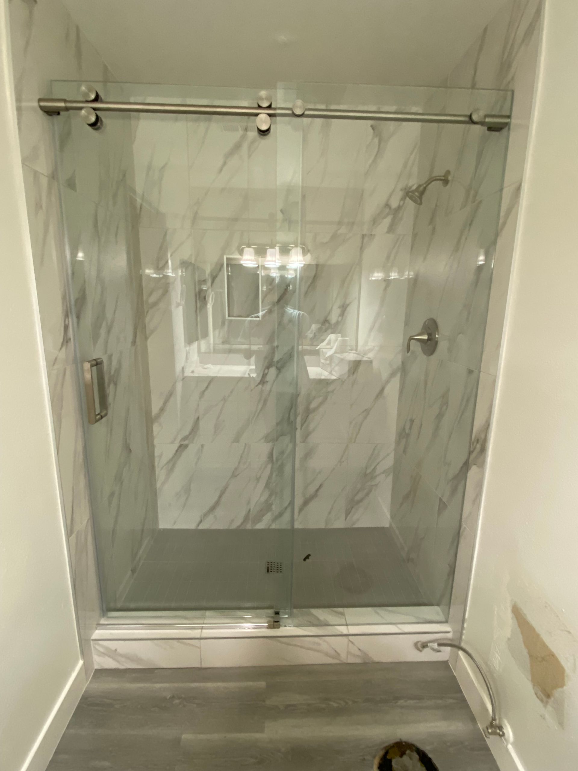 Glass shower with sliding door, marble tile walls, and silver hardware.