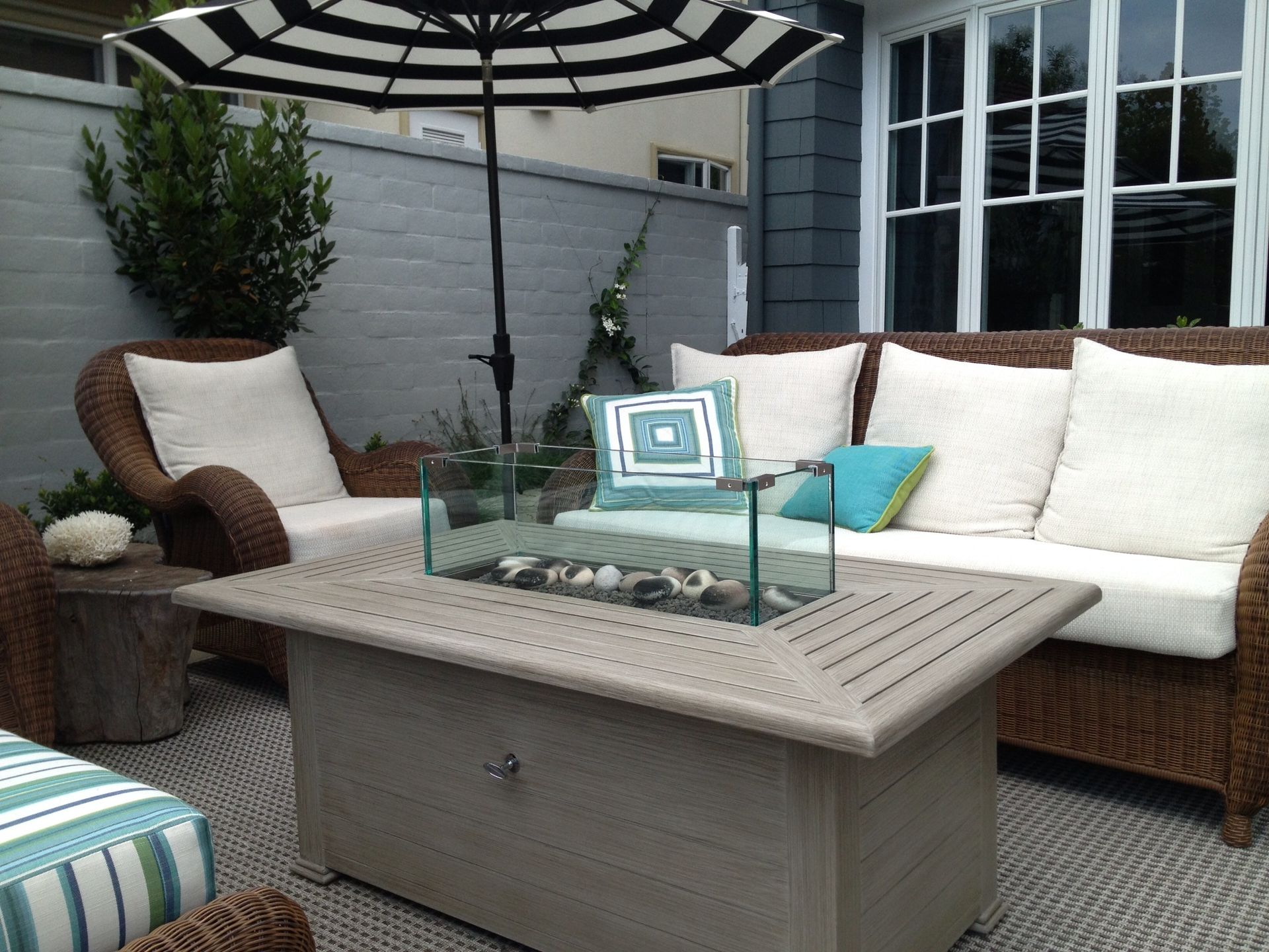Patio seating with a gas fire pit, striped umbrella, and white cushions.