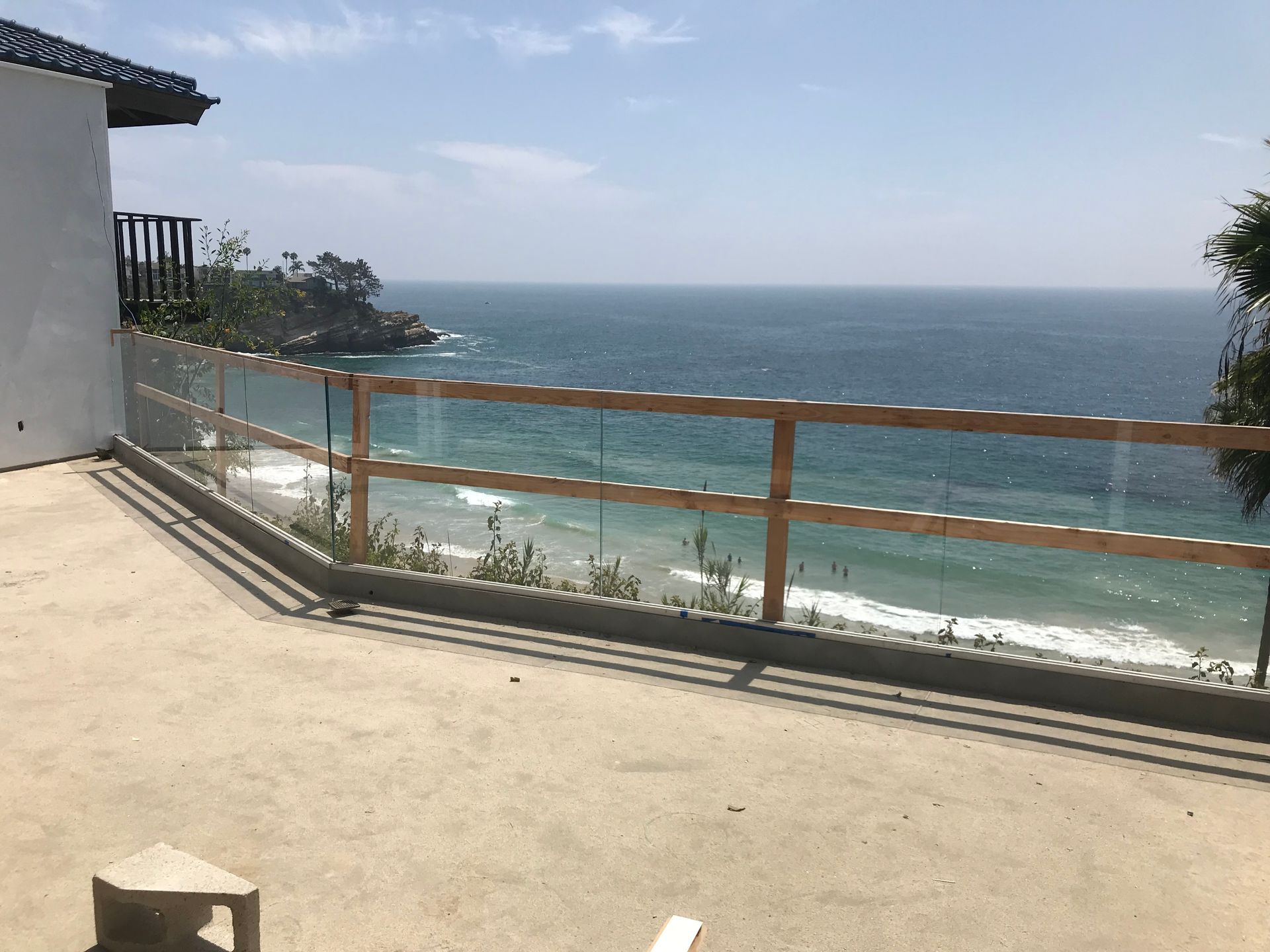 Ocean view from a terrace with a glass and wood railing, on a sunny day.