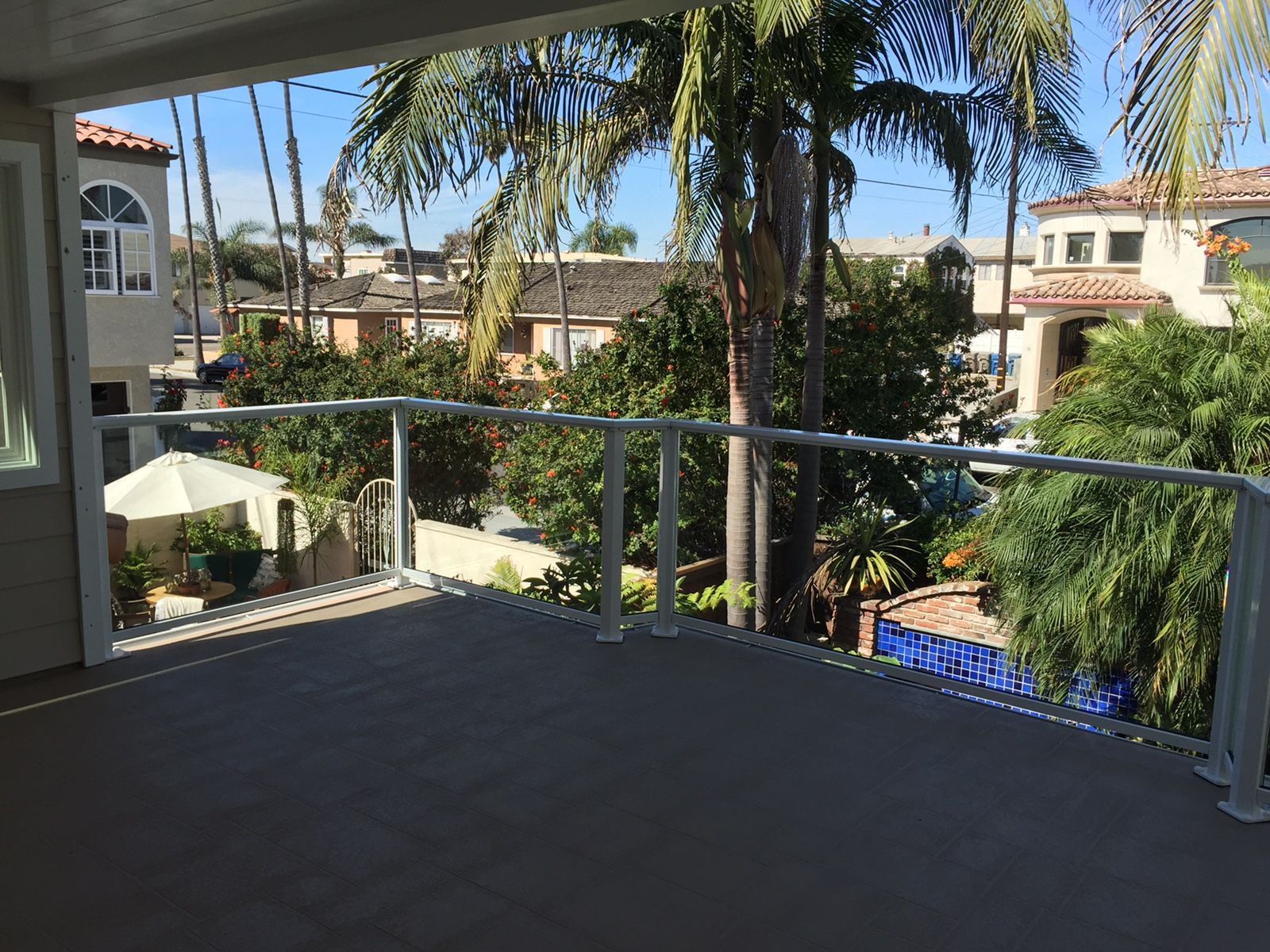 Balcony overlooking a street with palm trees and houses, featuring glass and white railing.
