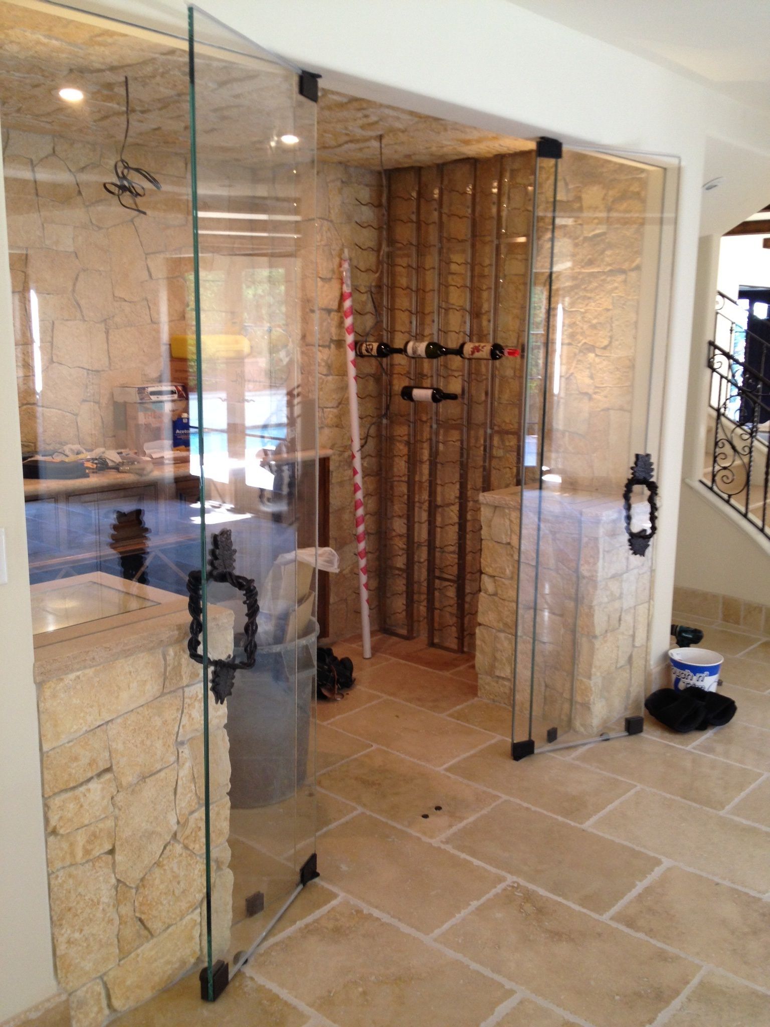 Glass-enclosed wine cellar with stone walls and a stone floor, accessed by glass doors.