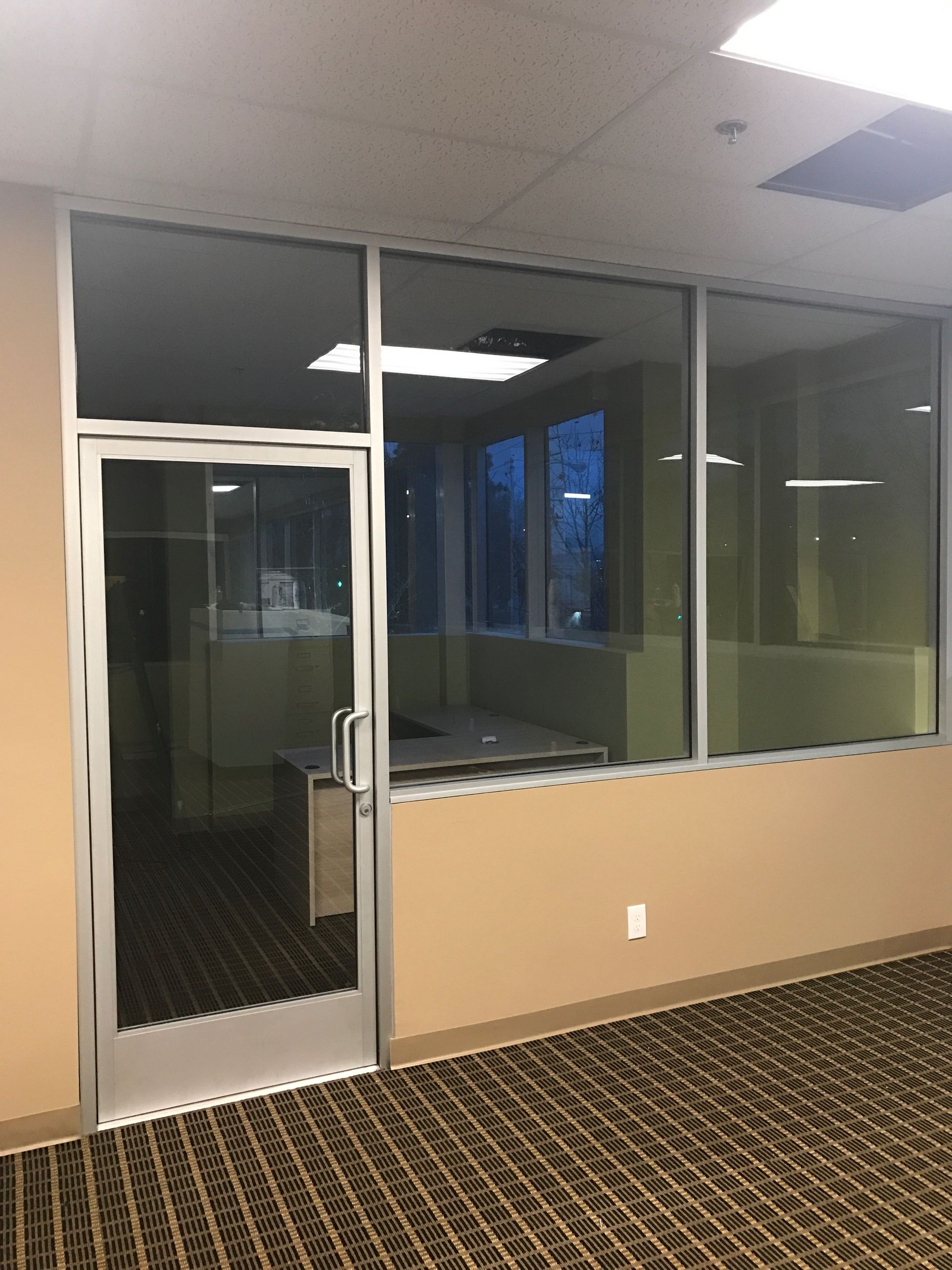 Office interior with glass door and windows, tan walls, and carpet.
