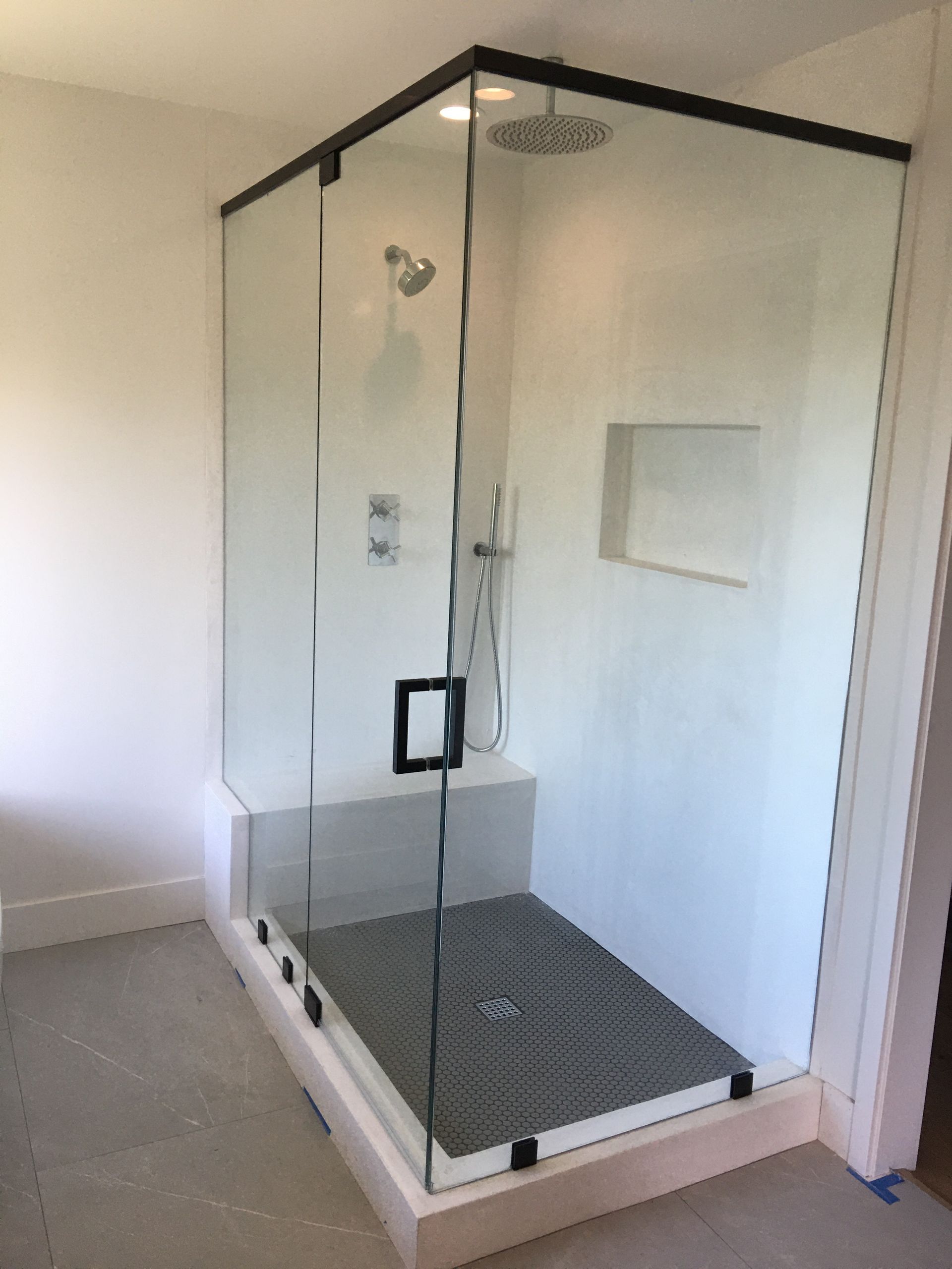 Glass shower enclosure with black trim, gray floor, white walls and a built-in shelf.