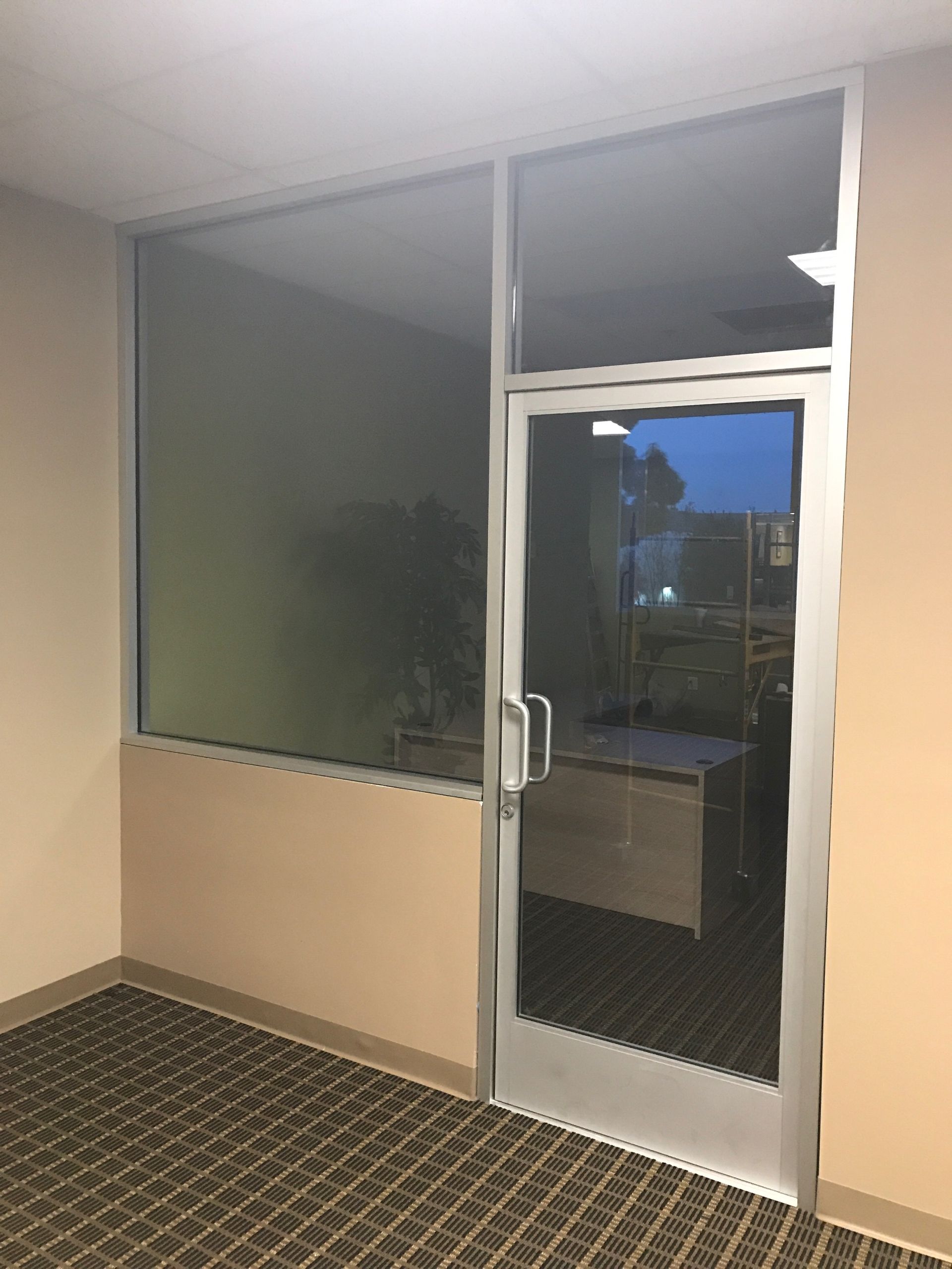 Office entrance with glass door and sidelight. Beige walls, carpeted floor. Door handle visible.