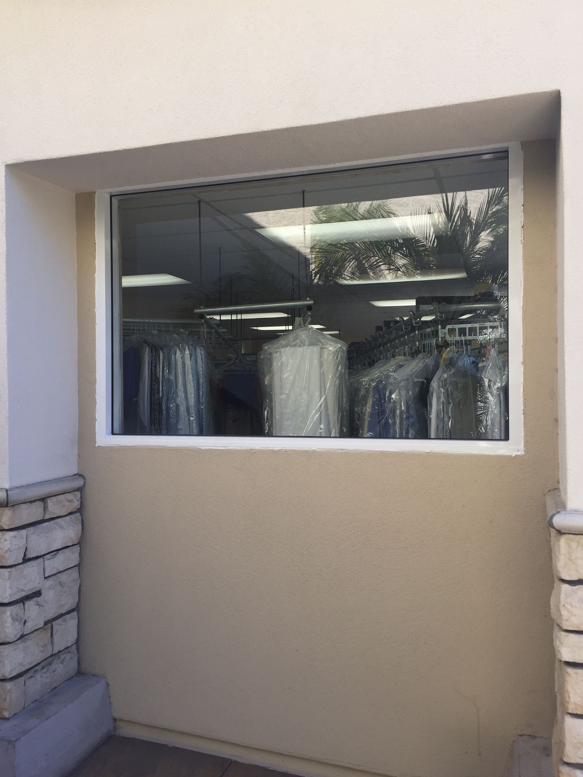Window into a dry cleaner showing wrapped garments on racks; the wall is beige with white trim.