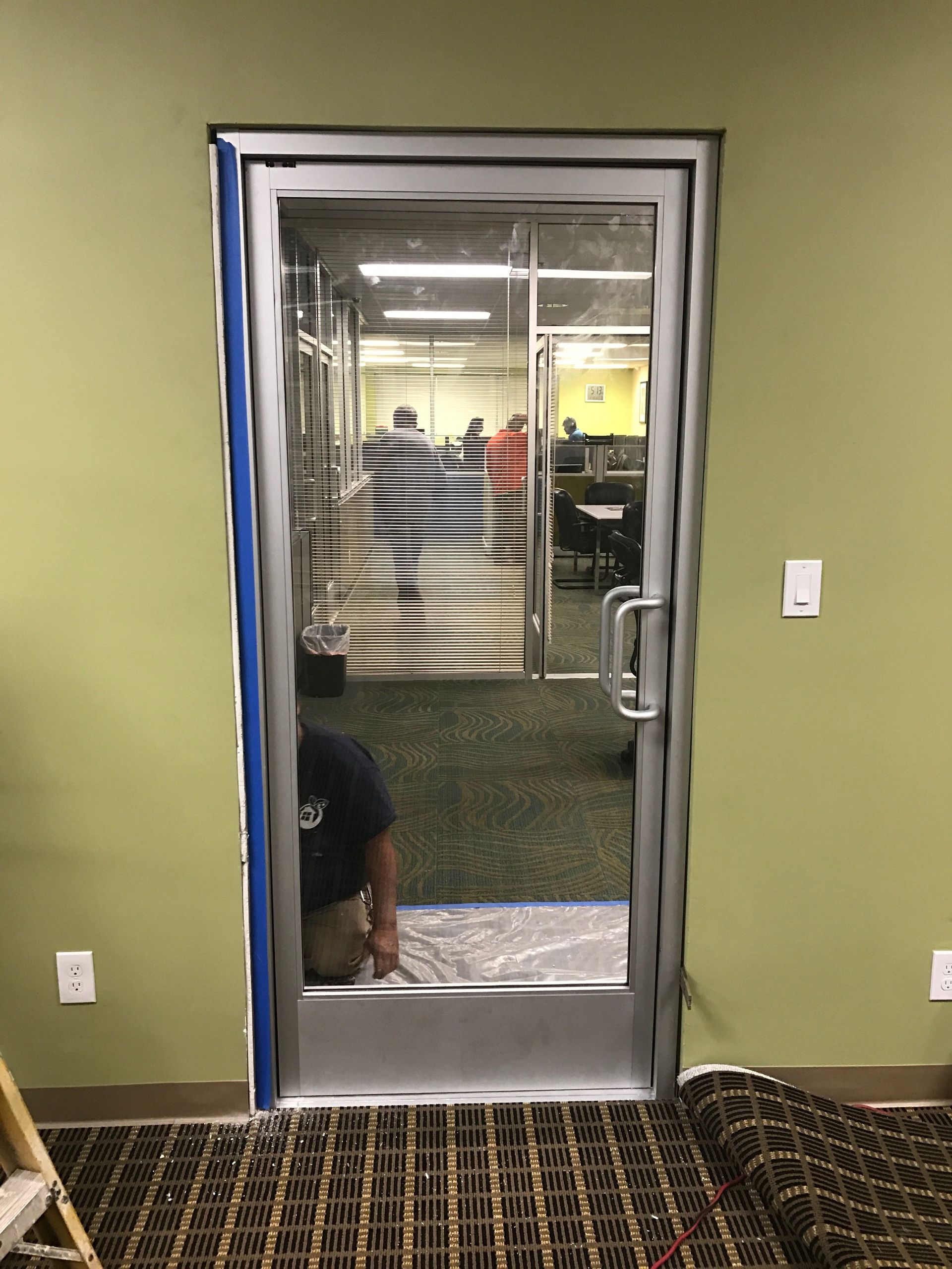 Glass door with silver frame, blue tape around the edges. Person crouched near the bottom, looking through the door.
