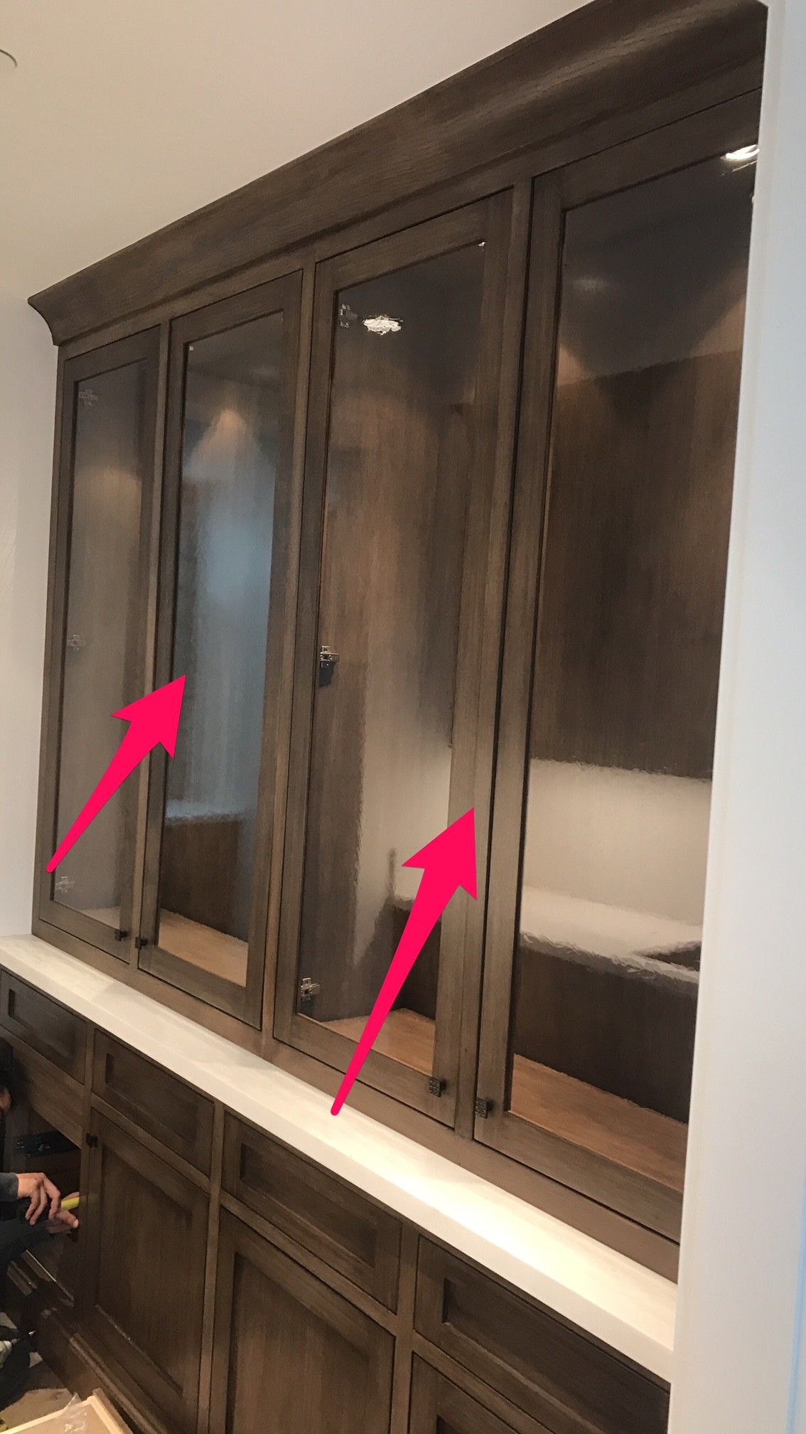 Wooden cabinets with glass doors, arrows pointing to the doors, built into a wall.