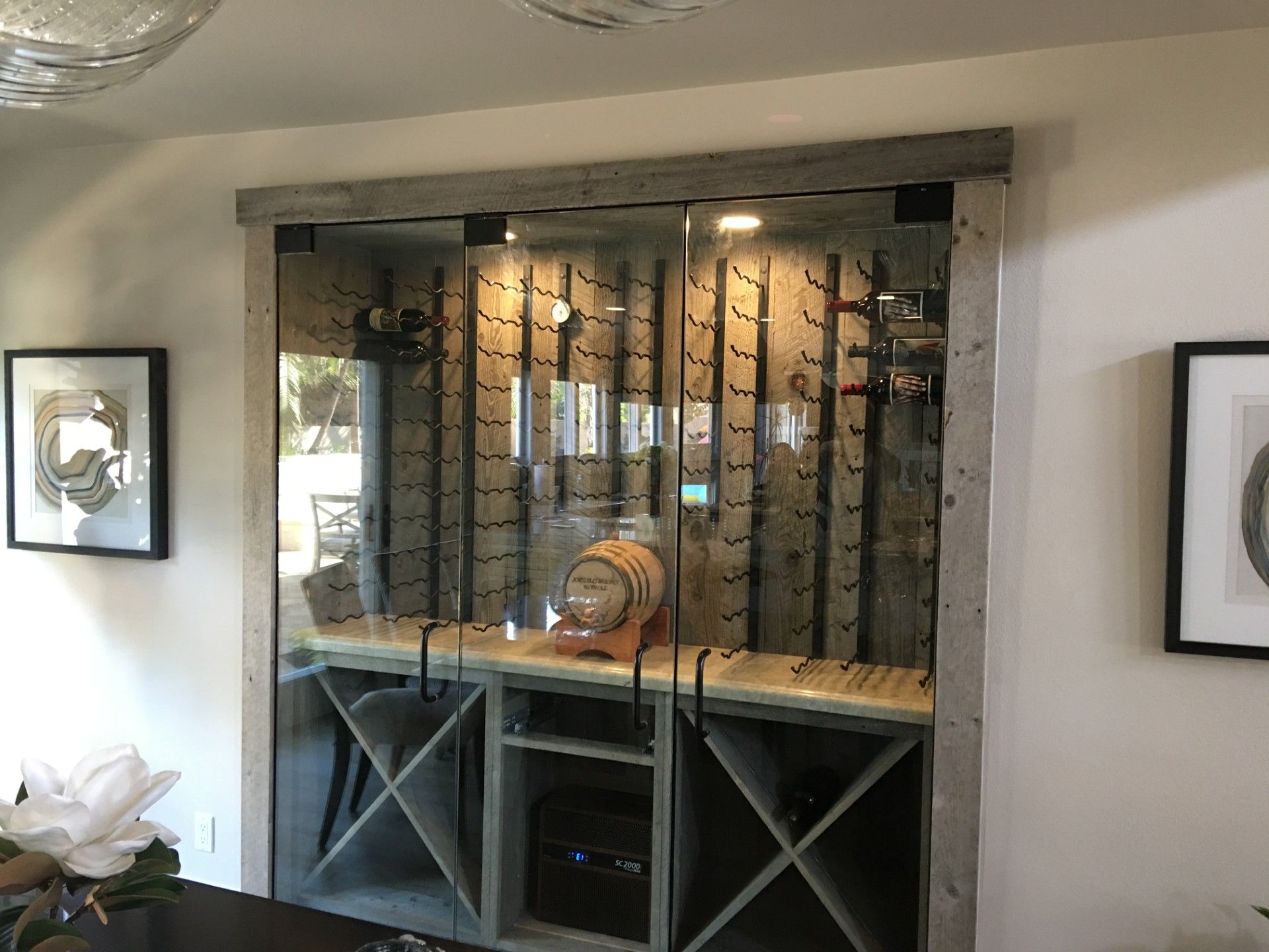 Wine cellar with glass doors, stone trim, and wood racks, holding bottles and a barrel.