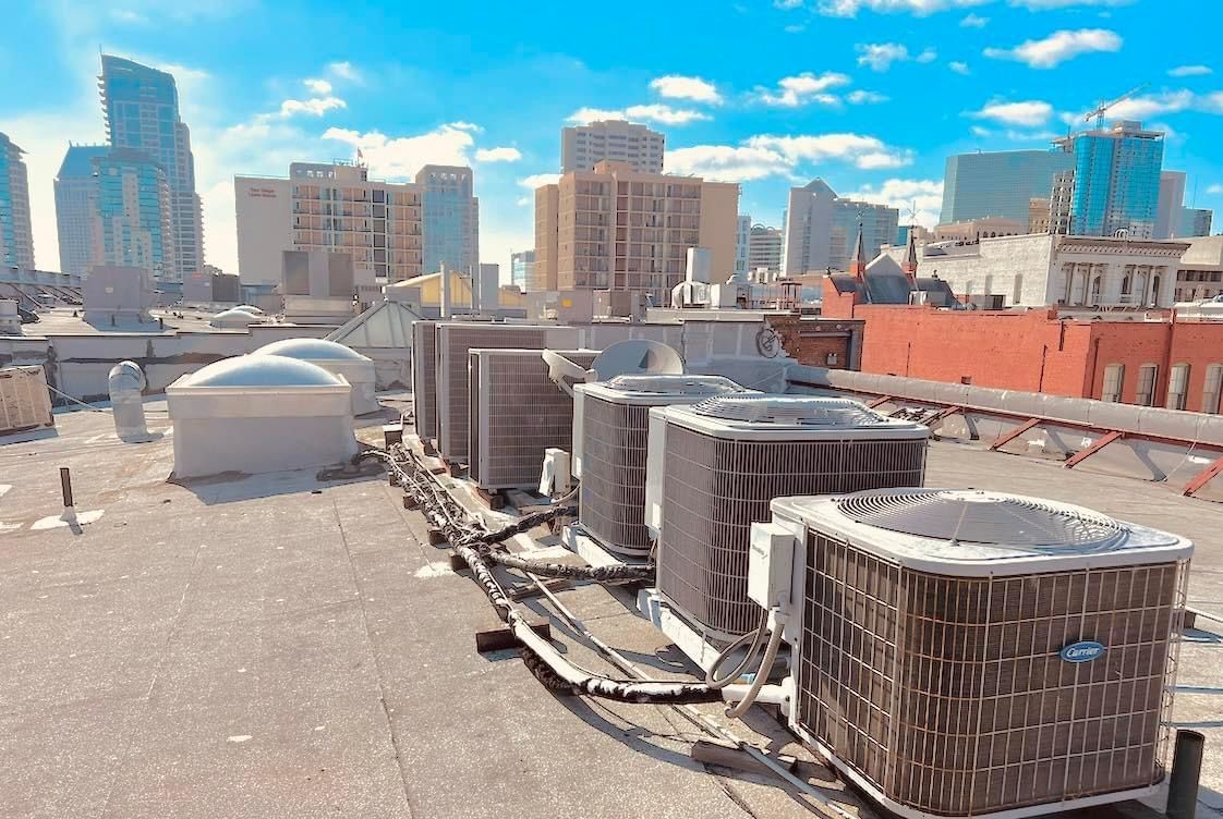 A row of air conditioners on the roof of a building with a city skyline in the background.