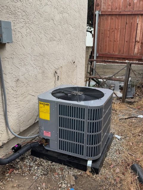 An air conditioner is sitting outside of a building next to a fence.
