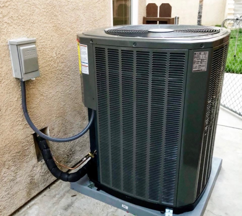 An air conditioner is attached to a wall outside of a house.