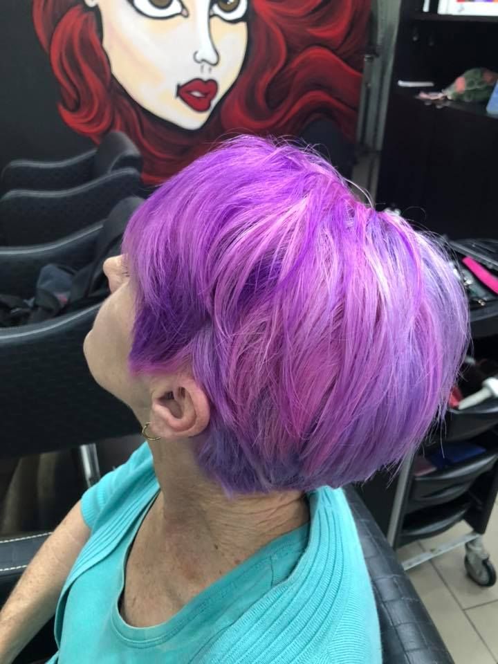 A Woman with Purple Hair Is Sitting in A Chair in Front of A Painting of A Woman 's Face — Hair It Is In Balgownie, NSW