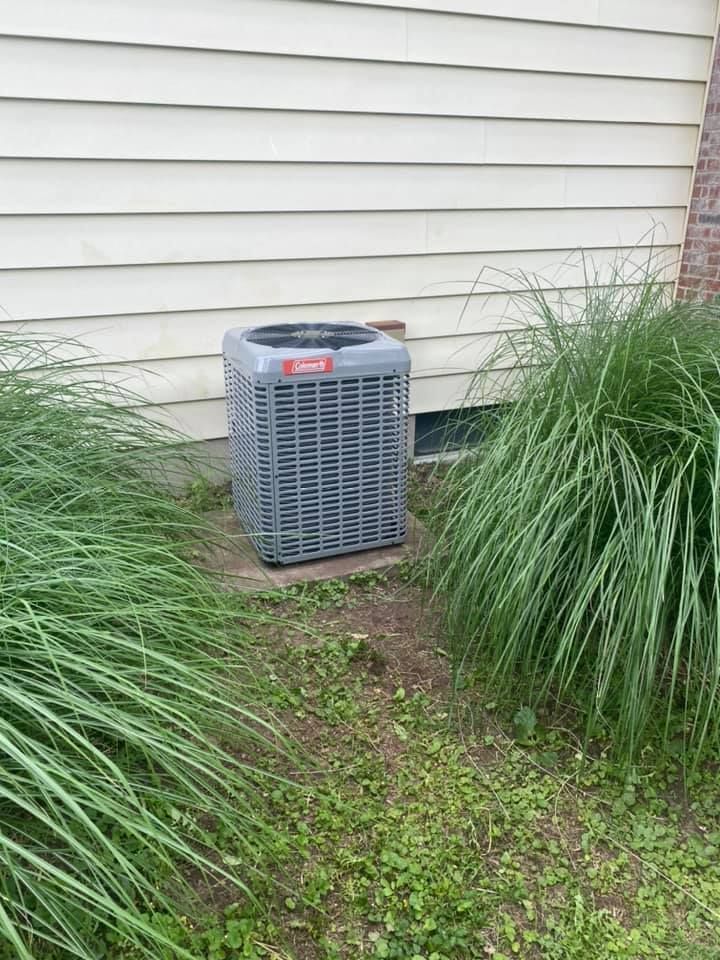 A large air conditioner is sitting in the grass next to a house.