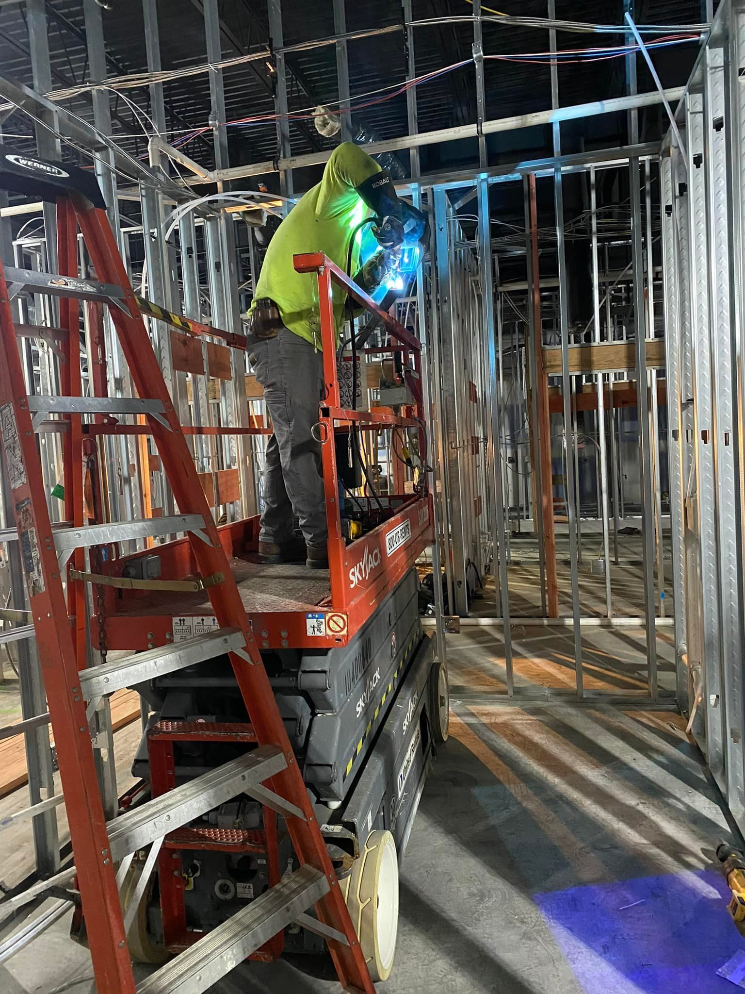 A man is welding on a scissor lift in a building under construction.